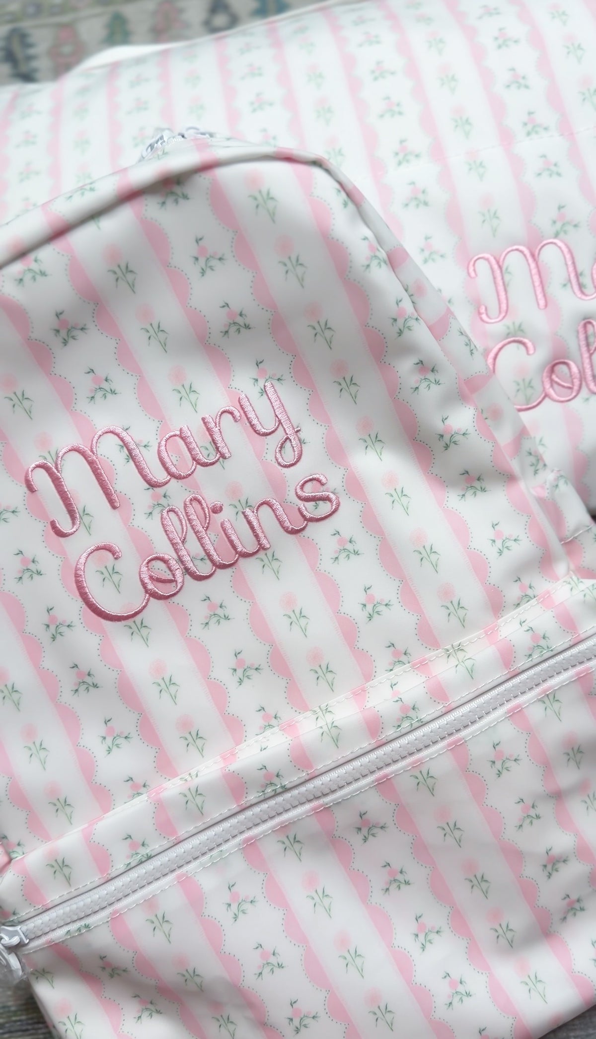 Close-up of pink ribbon floral striped backpack embroidered with the name 'Mary Collins' in pink script