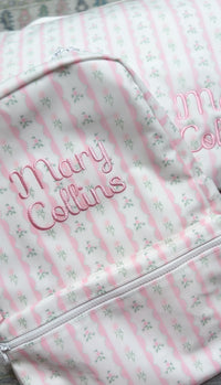Close-up of pink ribbon floral striped backpack embroidered with the name 'Mary Collins' in pink script