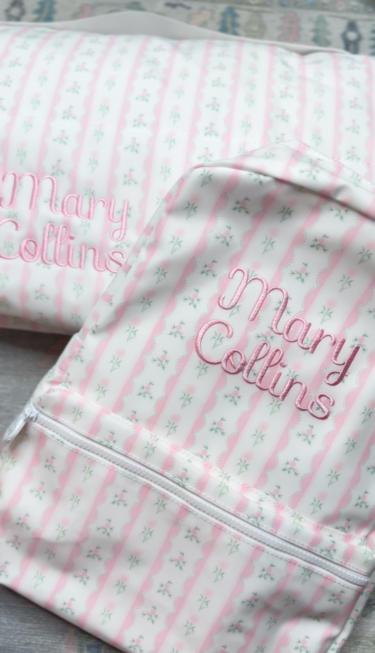 Pink ribbon floral striped backpack embroidered with the name 'Mary Collins' in pink script, close-up view