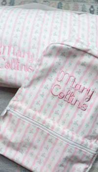 Pink ribbon floral striped backpack embroidered with the name 'Mary Collins' in pink script, close-up view