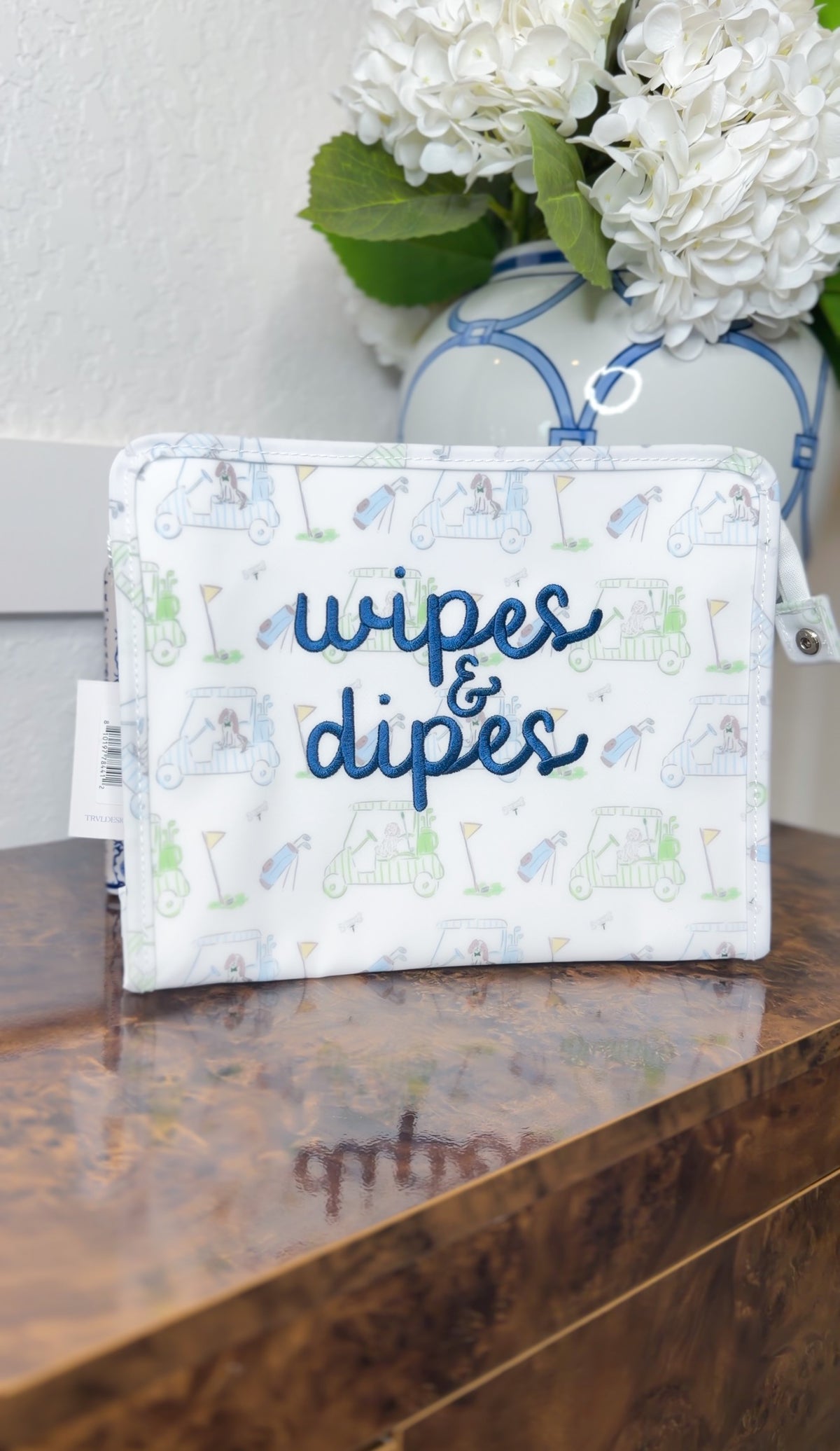 White TRVL pouch with blue golf cart print, embroidered 'wipes & dipes' in navy cursive