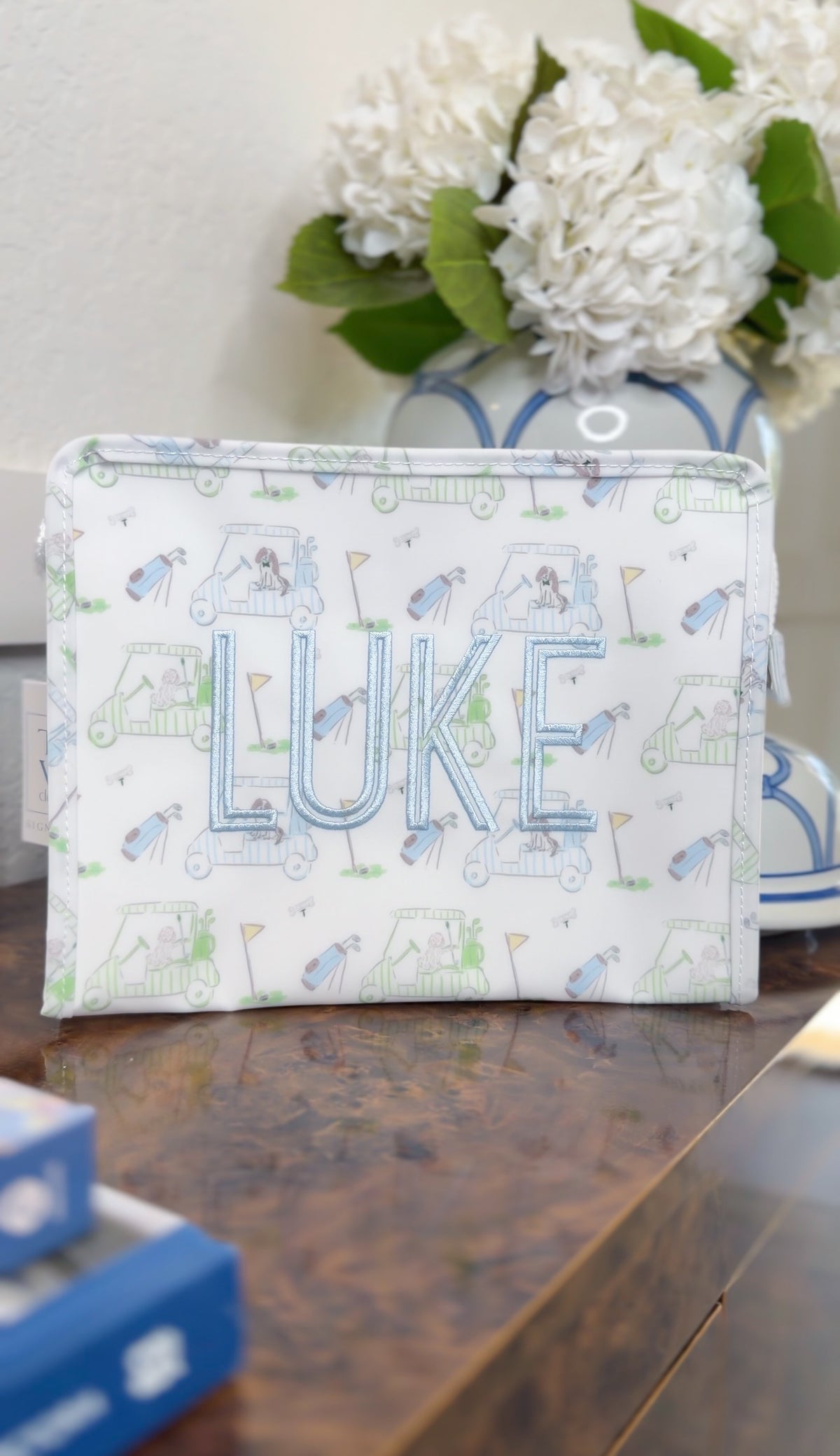White TRVL pouch with blue golf print, embroidered with the name 'Luke'