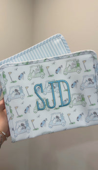 White TRVL pouch with blue golf print embroidered 'SJD' monogram, layered with a blue striped pouch