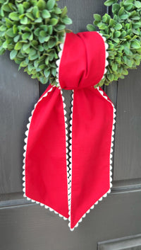 Red bow with white trim on a door with green wreaths.