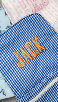 Royal blue gingham TRVL Backpacker embroidered with the name 'Jack' in orange, next to a pink floral bag