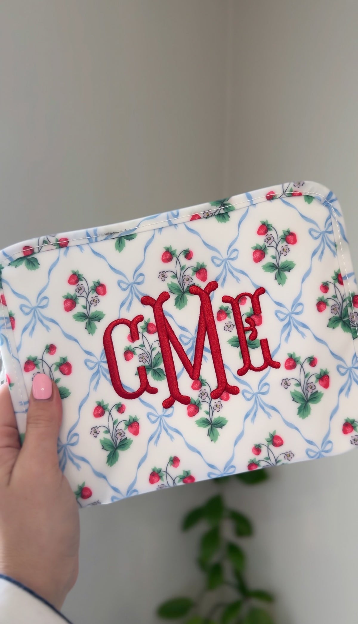 White TRVL pouch with strawberry and bow print, embroidered with the red 'GME' monogram