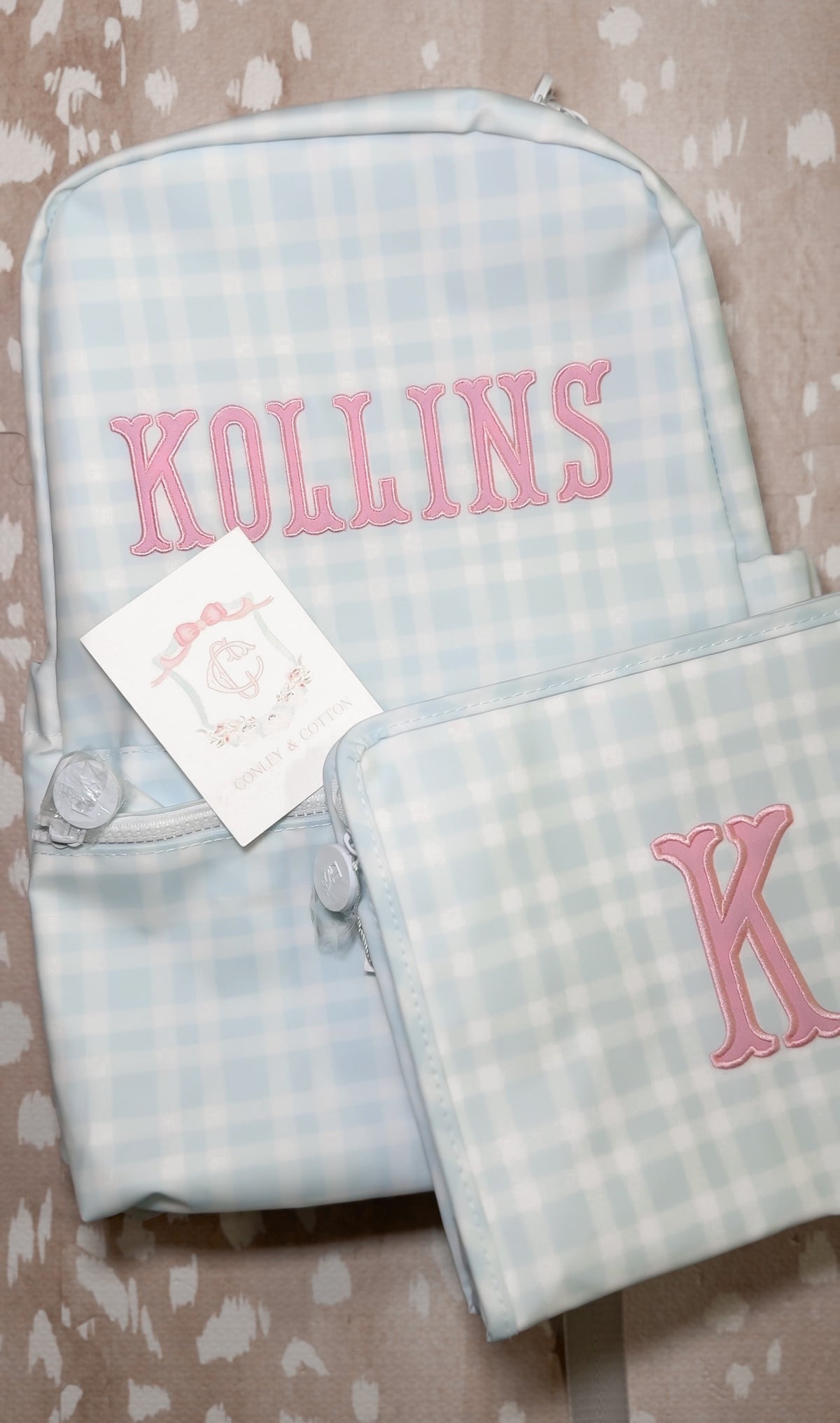 Light blue plaid TRVL backpack and pouch embroidered with the name 'Kollins' in pink