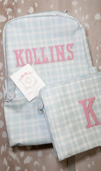 Light blue plaid TRVL backpack and pouch embroidered with the name 'Kollins' in pink