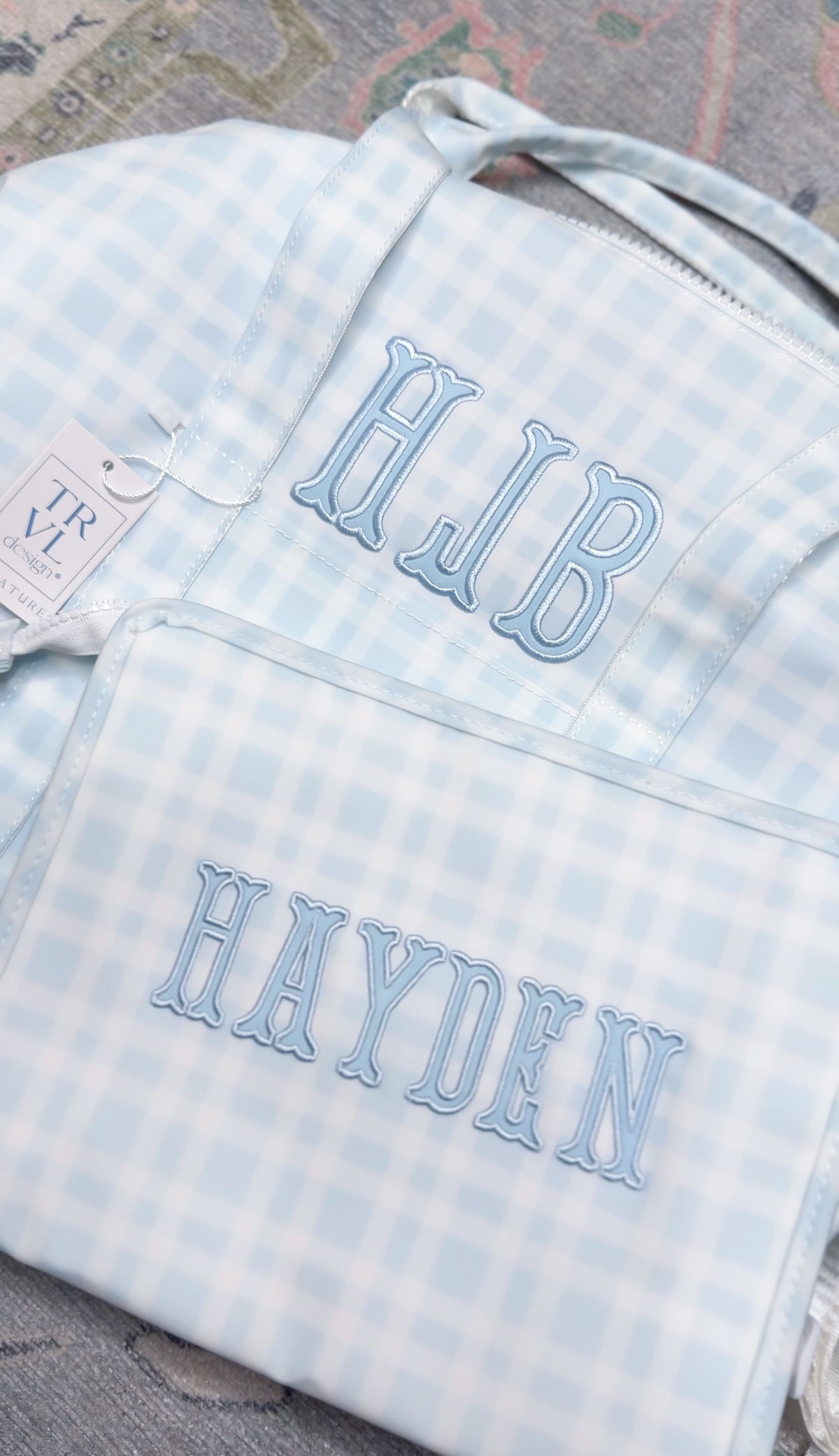 Light blue plaid TRVL bag and pouch embroidered with the 'HJB' monogram and the name 'Hayden'
