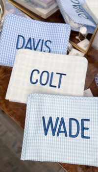 Light blue gingham and plaid TRVL pouches embroidered with the names Davis, Colt, and Wade