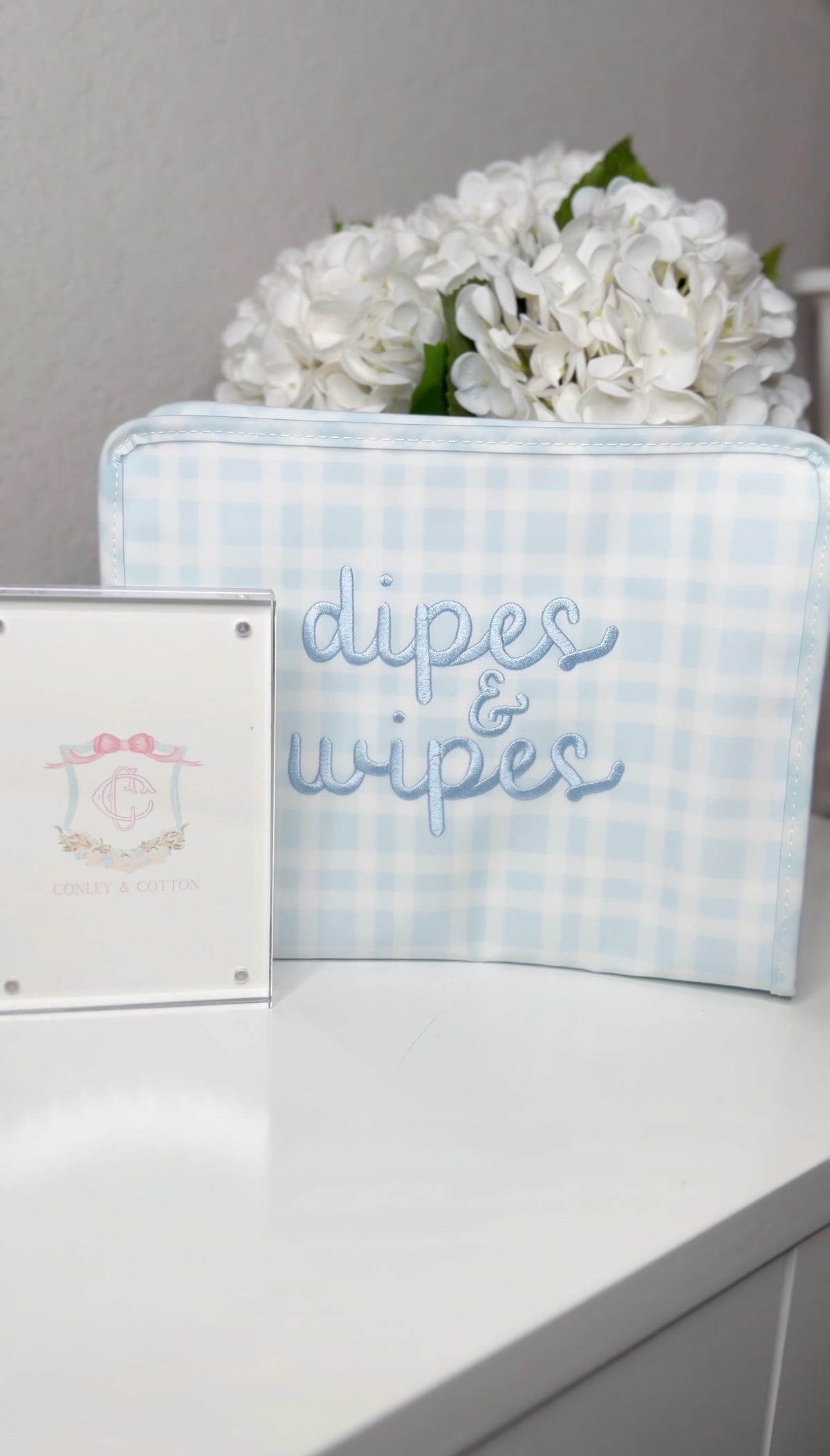 Light blue gingham TRVL pouch embroidered 'dipes & wipes' in blue script