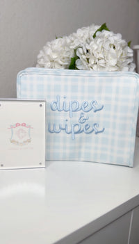 Light blue gingham TRVL pouch embroidered 'dipes & wipes' in blue script