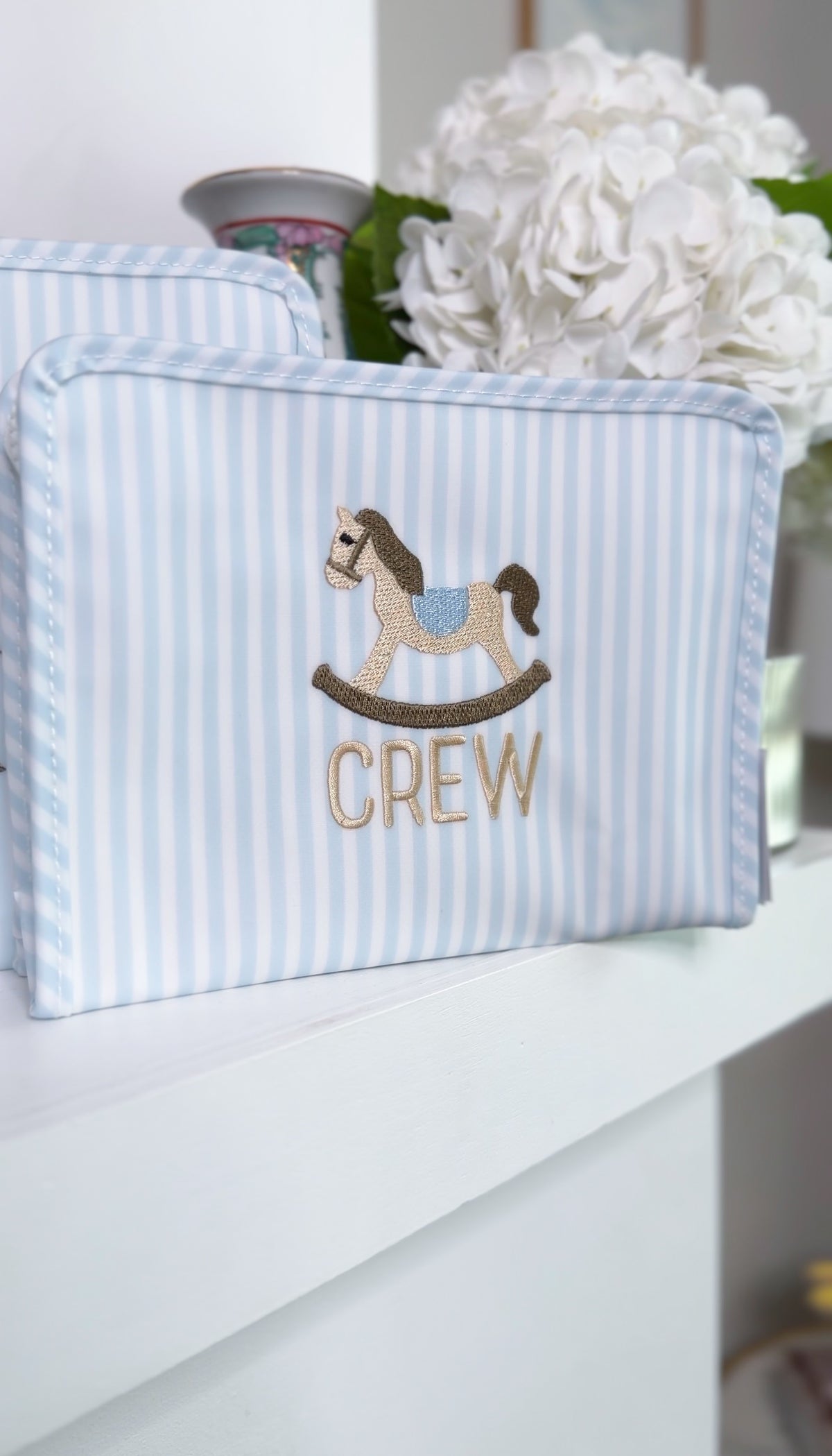 Blue and white striped TRVL Roadie pouch embroidered with a rocking horse design and 'CREW' text