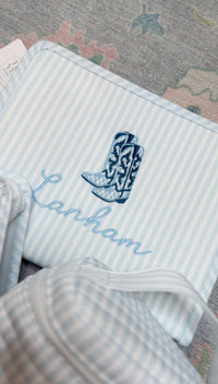 Blue and white striped TRVL Roadie pouch embroidered with a cowboy boot design and 'Lanham' in cursive script