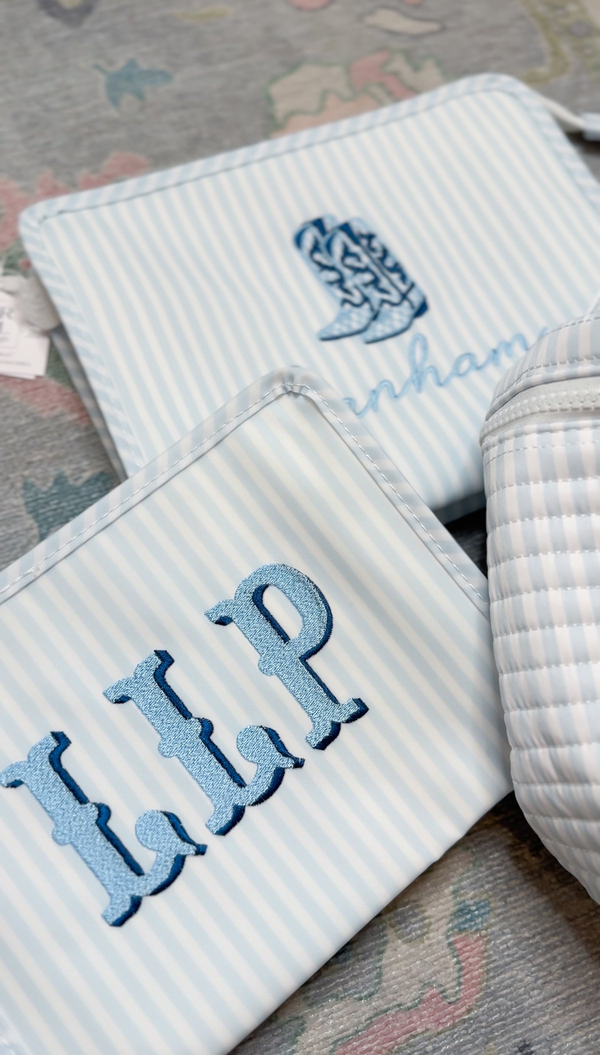 Two blue and white striped TRVL Roadie pouches, one embroidered with a cowboy boot design and name, the other with 'LLP' monogram