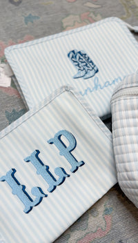 Two blue and white striped TRVL Roadie pouches, one embroidered with a cowboy boot design and name, the other with 'LLP' monogram