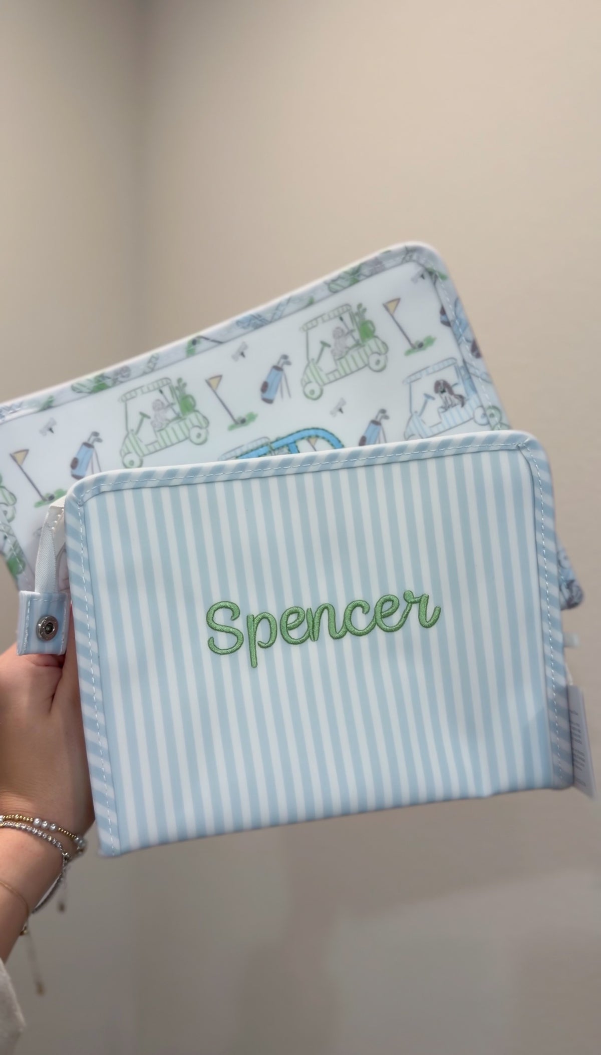 Blue and white striped TRVL Roadie pouch embroidered with 'Spencer' in green cursive script