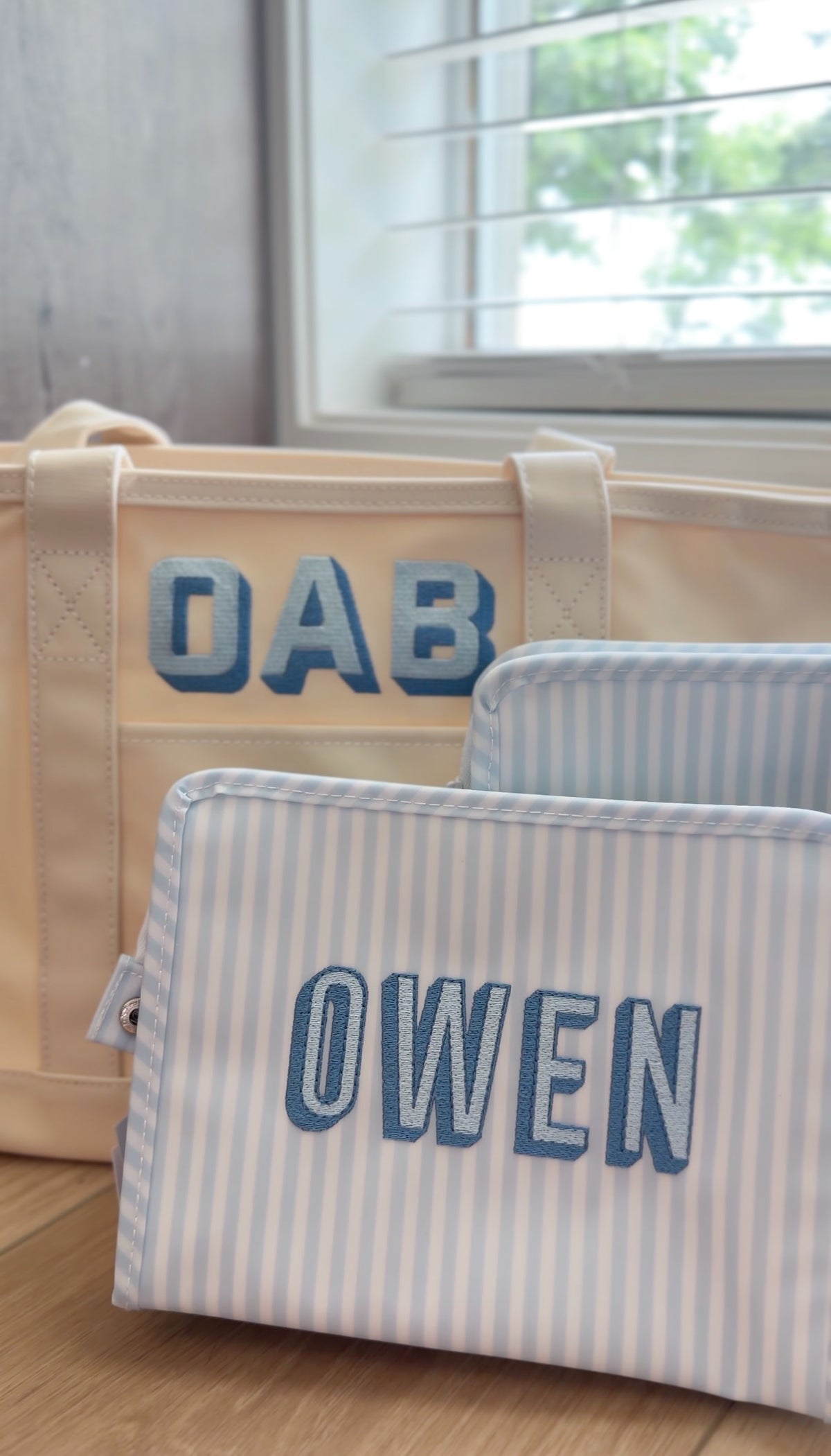 Blue and white striped TRVL Roadie pouch embroidered with 'OWEN' in bold block letters, shown with a matching tote bag