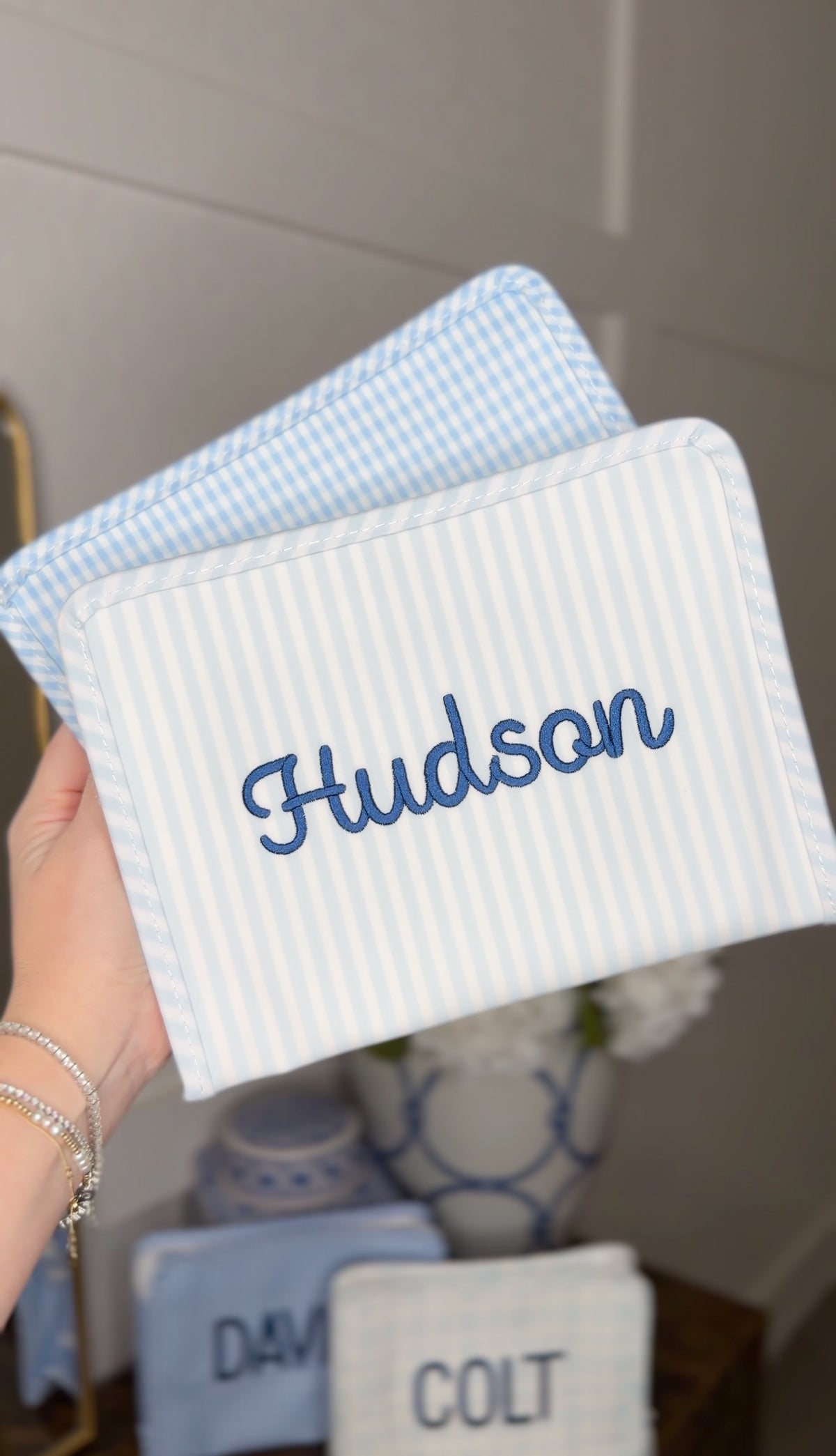 Blue Pimlico stripe TRVL Roadie pouch embroidered with 'Hudson' in cursive script, shown with other personalized pouches
