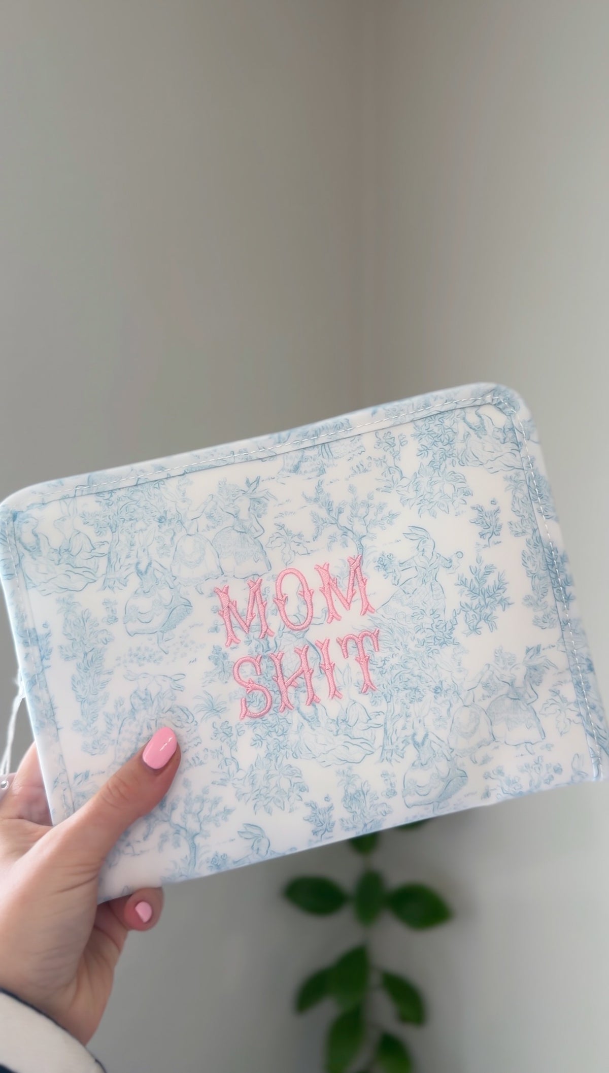 Blue bunny toile TRVL pouch embroidered with pink text reading 'Mom Sh*t'