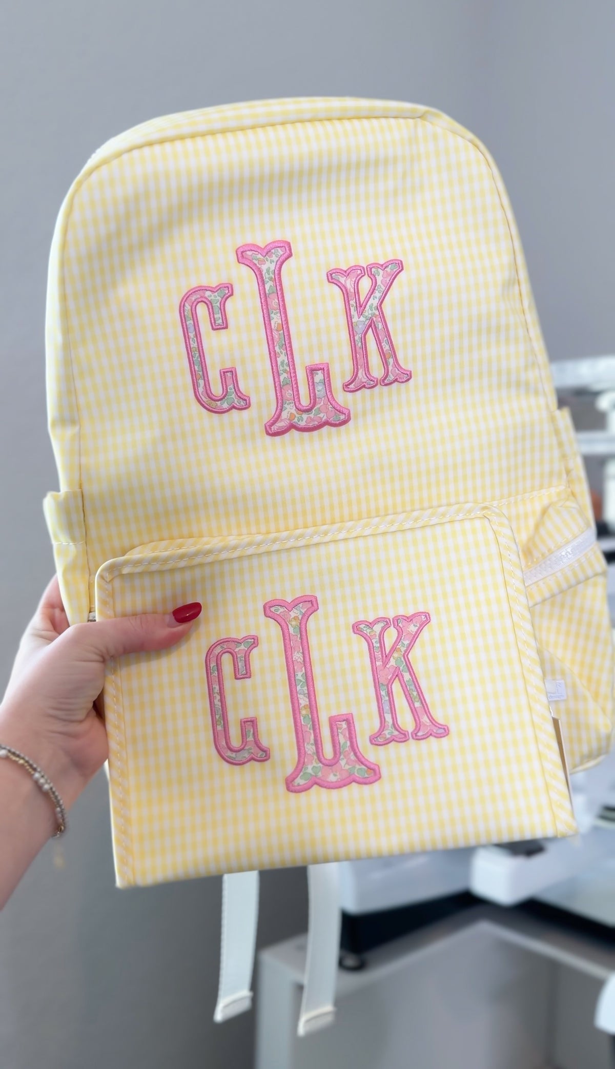 Yellow gingham TRVL backpack and matching pouch both embroidered with a pink and floral 'CLK' monogram