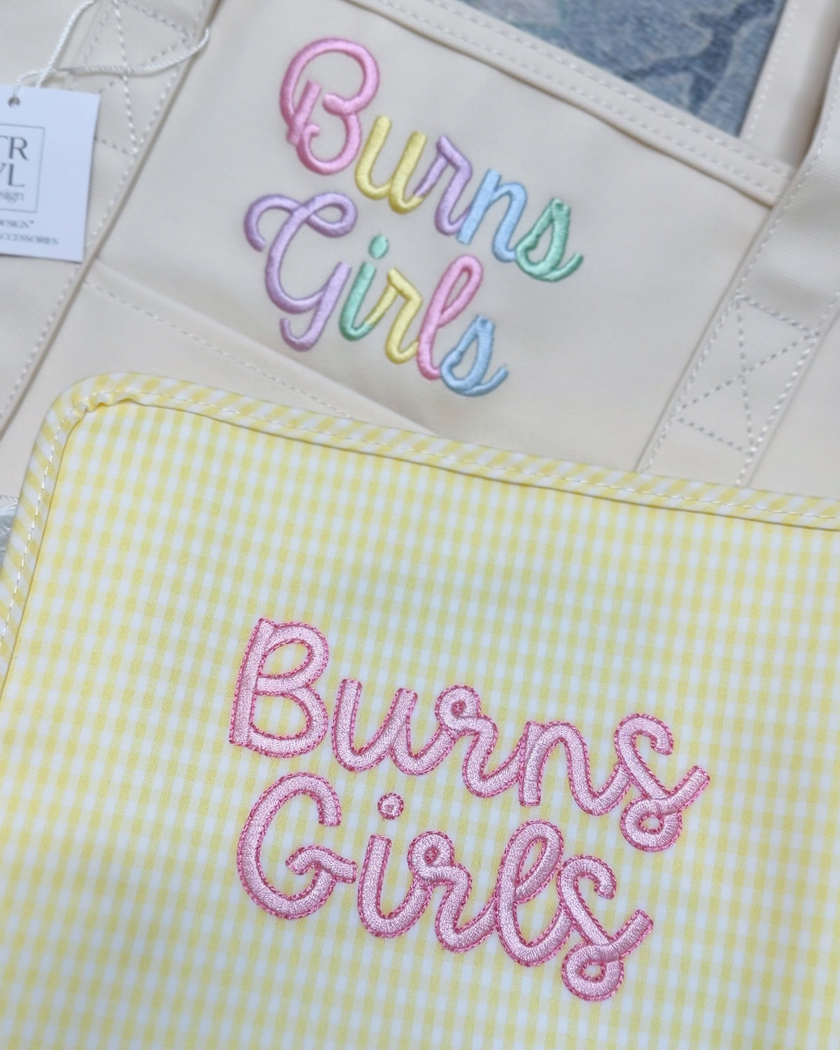 Cream and yellow gingham TRVL pouches embroidered with 'Burns Girls' in pastel and pink script lettering