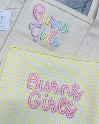Cream and yellow gingham TRVL pouches embroidered with 'Burns Girls' in pastel and pink script lettering