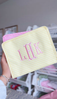 Yellow gingham TRVL pouch embroidered with a pink 'LHK' monogram, layered next to a pink gingham pouch