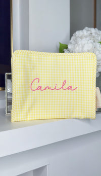 Yellow gingham TRVL Roadie pouch embroidered with the name 'Camila' in pink script, displayed on a mantel with hydrangeas