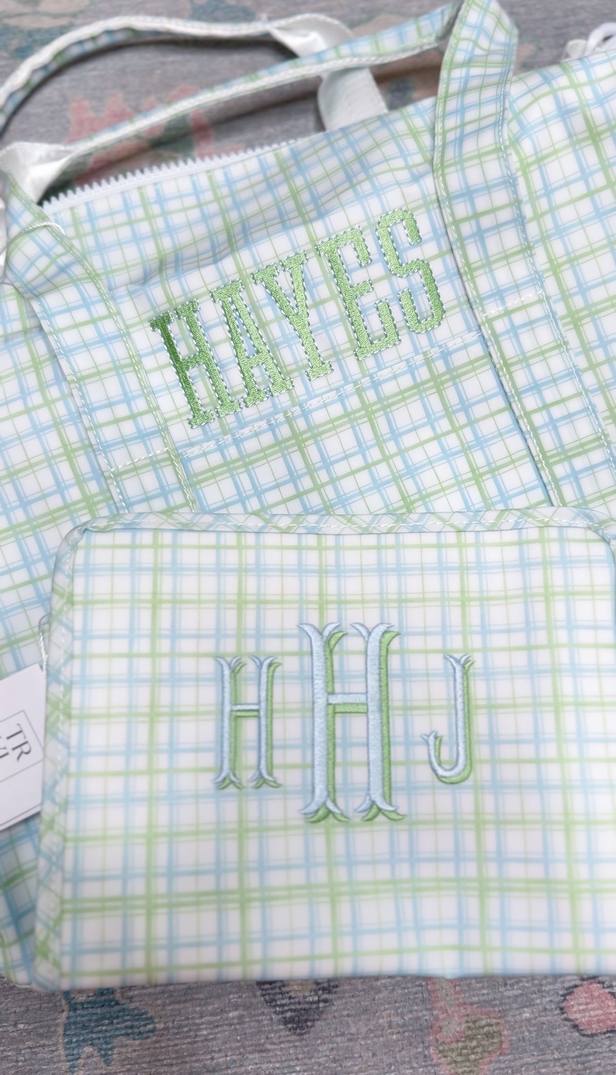 Green and blue plaid TRVL duffel and pouch, embroidered with the name 'Hayes' and the 'HHJ' monogram