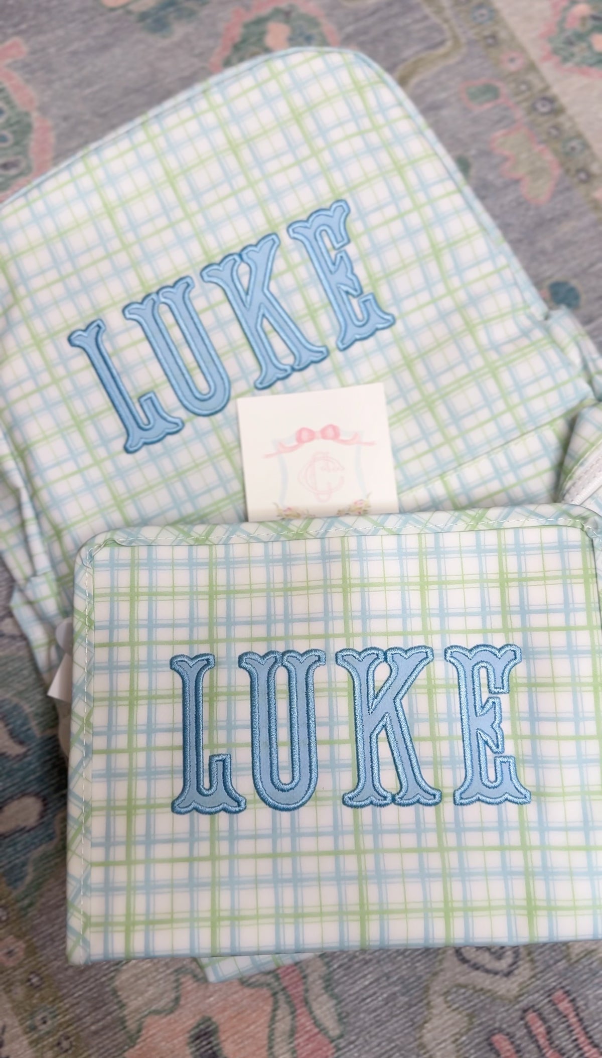 Green and blue plaid TRVL backpack and pouch both embroidered with the name 'Luke'