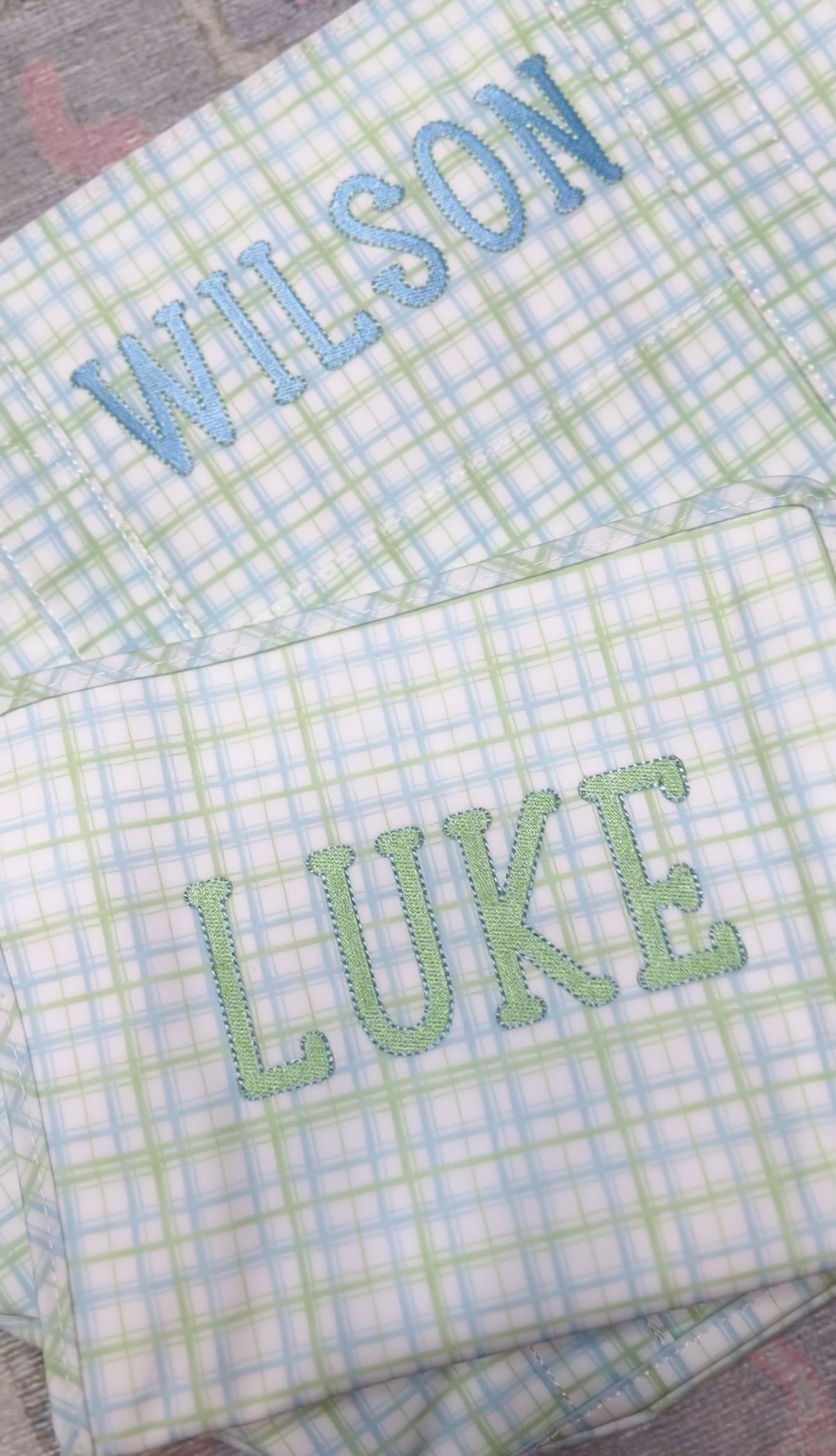 Green and blue plaid TRVL pouches embroidered with the names 'Wilson' and 'Luke'