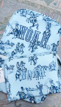 Light blue cowboy toile TRVL Backpacker and matching pouch, both embroidered with the name 'Noah'