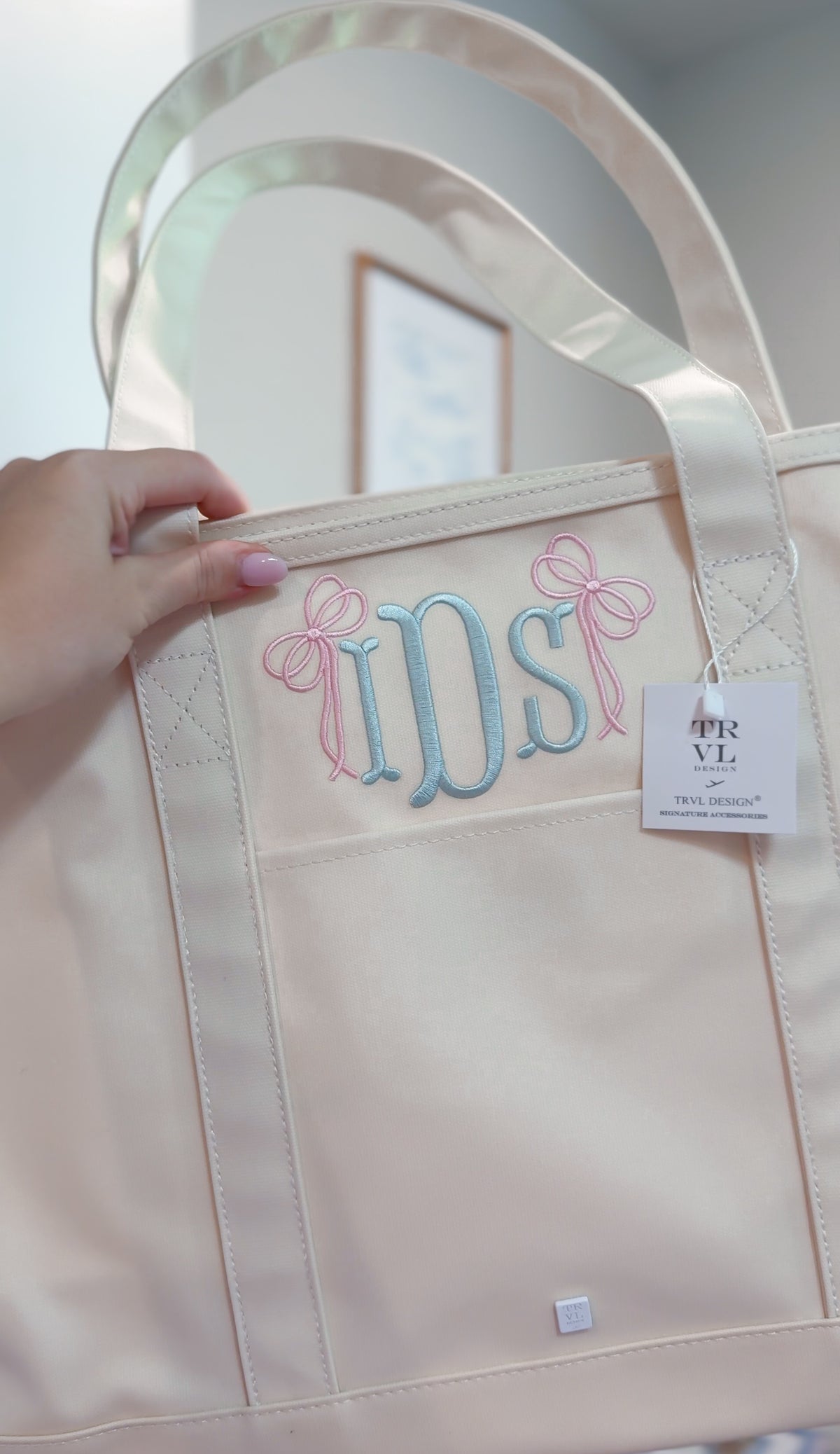 Natural canvas TRVL Maxi Tote held up, embroidered with a pink and blue bow monogram