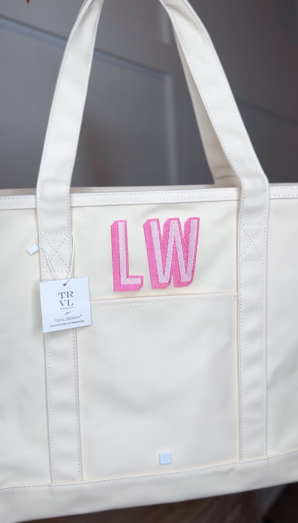 Natural canvas TRVL Maxi Tote with a TRVL Designs tag, embroidered with a pink 'LW' monogram
