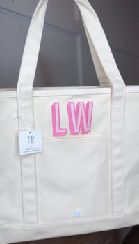 Natural canvas TRVL Maxi Tote with a TRVL Designs tag, embroidered with a pink 'LW' monogram