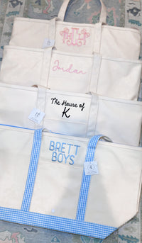 Four natural canvas TRVL Maxi Totes stacked, embroidered with a pink bow monogram, 'Jordan' in script, 'The House of K', and 'Brett Boys' in blue with gingham handles