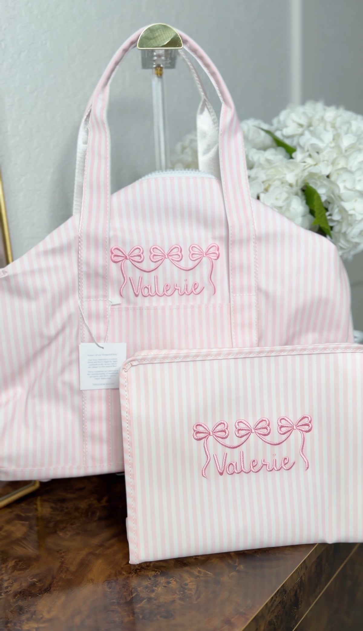 Pink Pimlico stripe TRVL Roadie pouch embroidered with a bow design and 'Valerie' in cursive script, shown with a matching tote bag