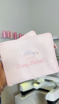 Pink Pimlico stripe TRVL Roadie pouches embroidered with a dinosaur design and 'Mary Micheal' in cursive script