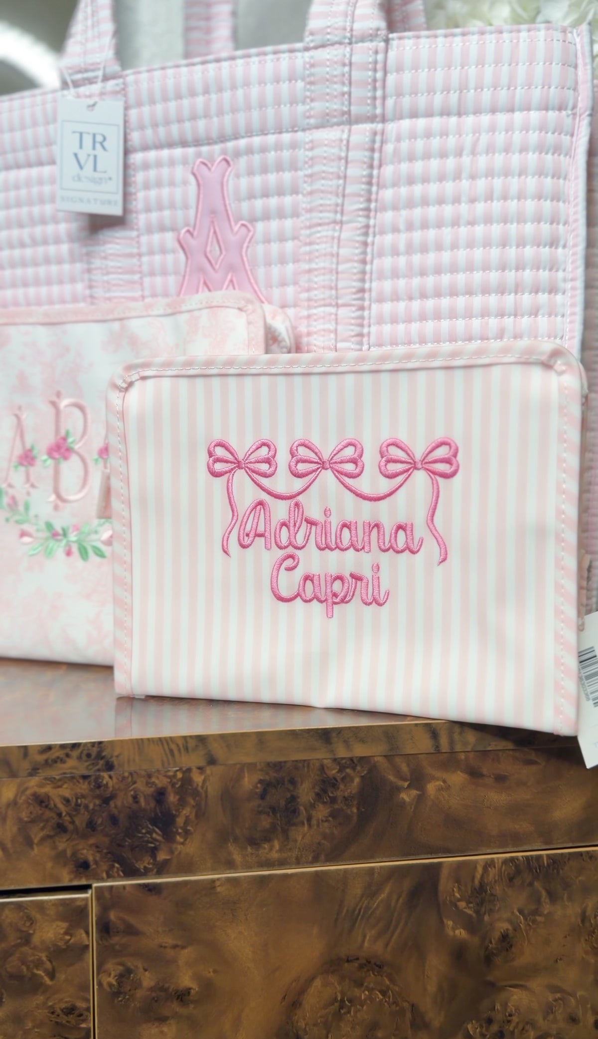 Pink Pimlico stripe TRVL Roadie pouch embroidered with a bow design and 'Adriana Capri' in cursive script