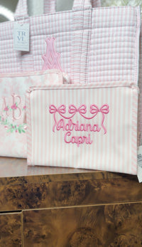 Pink Pimlico stripe TRVL Roadie pouch embroidered with a bow design and 'Adriana Capri' in cursive script