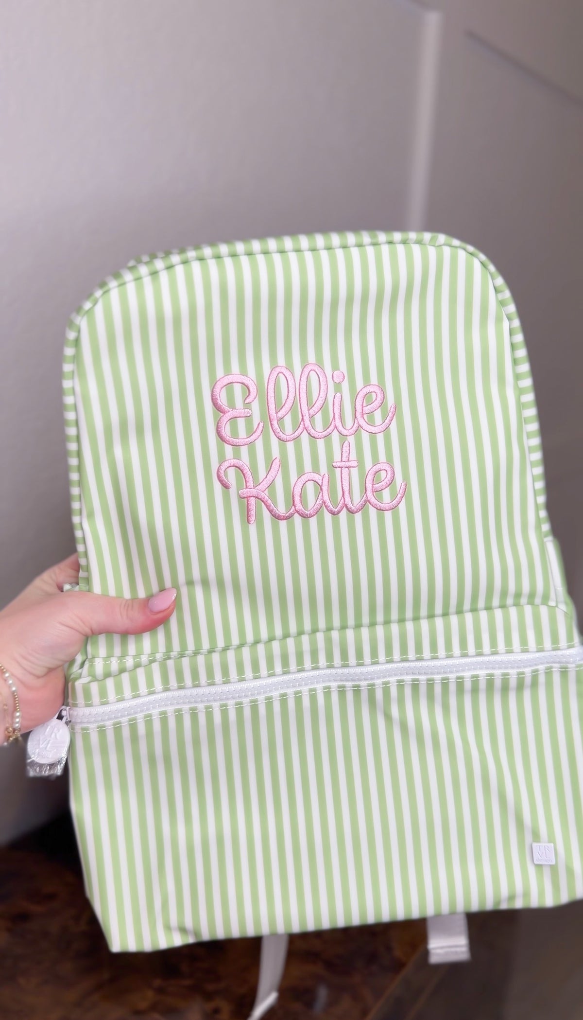 Green and white striped TRVL Backpacker held up, embroidered with the name 'Ellie Kate' in pink script