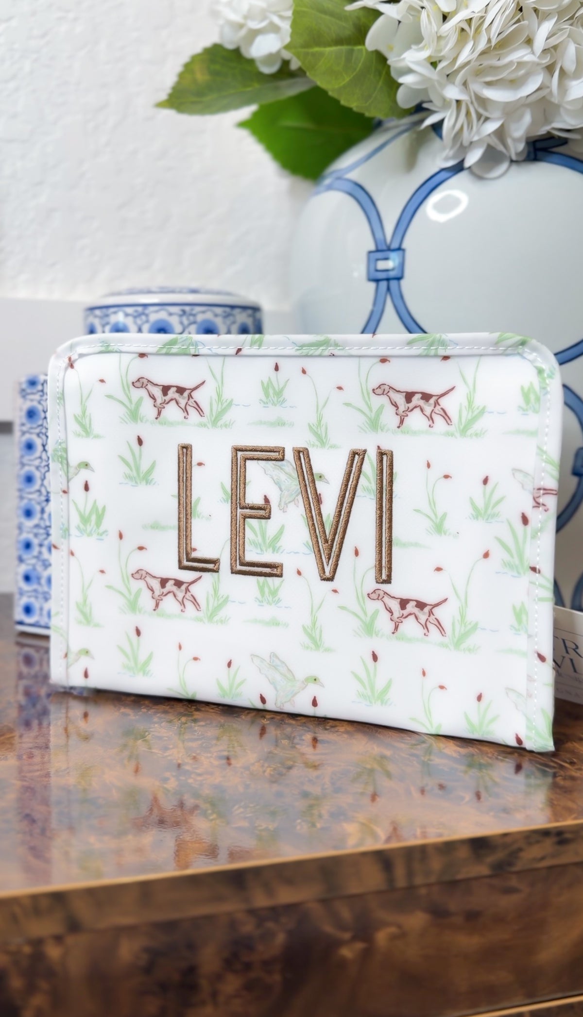 White TRVL Roadie pouch with green hunting dog print, embroidered with the name 'Levi'