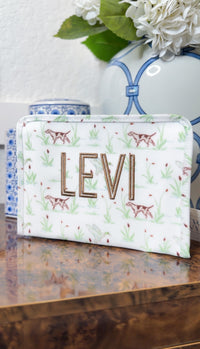White TRVL Roadie pouch with green hunting dog print, embroidered with the name 'Levi'