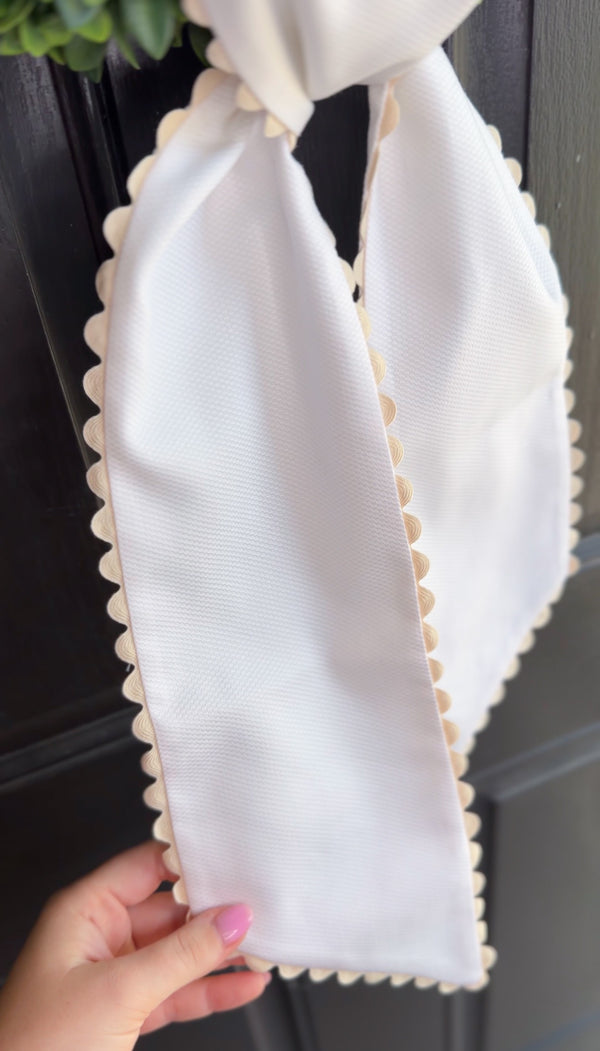 White wreath sash held by a hand against a dark background