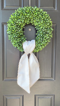 Green wreath with a white bow on a gray door