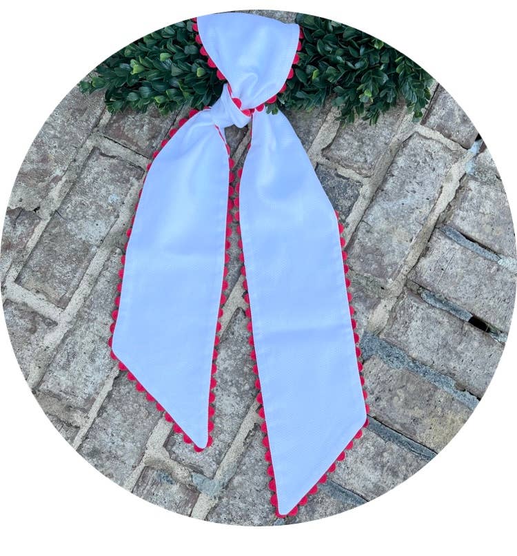 White cotton pique sash with red scalloped trim tied in a bow on a boxwood wreath, laid on a brick paver walkway