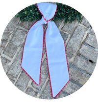 White cotton pique sash with red scalloped trim tied in a bow on a boxwood wreath, laid on a brick paver walkway