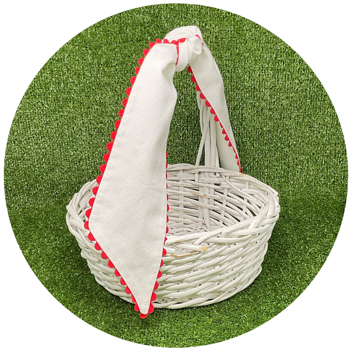 White cotton pique sash with red scalloped trim tied on a white wicker basket handle, styled on artificial turf