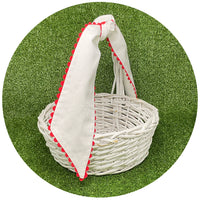 White cotton pique sash with red scalloped trim tied on a white wicker basket handle, styled on artificial turf